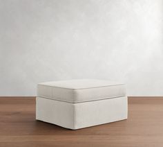 a white ottoman sitting on top of a wooden floor next to a wall and window