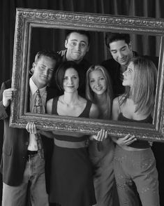 a group of people standing around each other in front of a photo booth holding up a frame