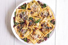 a white plate filled with pasta and spinach covered in cheese on top of a wooden table