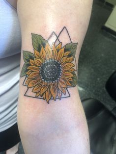 a sunflower tattoo on the arm with green leaves and black dots in it's center