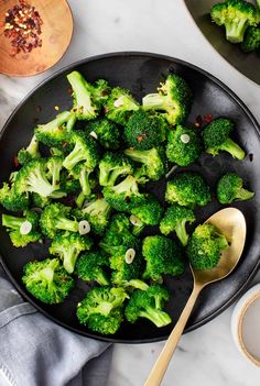 broccoli florets in a black bowl with spoons