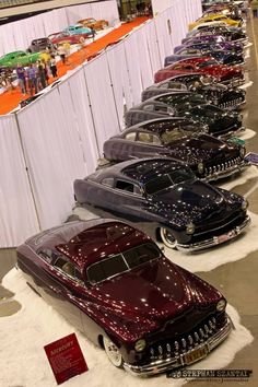 a row of classic cars parked next to each other in front of a white wall