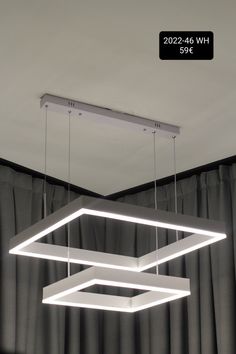 a suspended light fixture with three square lights hanging from it's sides, in front of curtains