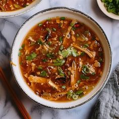 two bowls filled with soup next to chopsticks on a marble counter top,