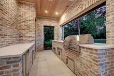 an outdoor kitchen with brick walls and grilling area next to the window that looks out onto the backyard