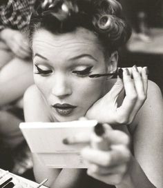 a black and white photo of a woman with eyeliners looking at her phone