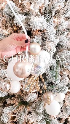 someone is decorating a christmas tree with white and gold ornaments on the top, while another hand holds an ornament