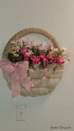 a wicker basket with pink and white flowers in it hanging on the wall next to a light switch