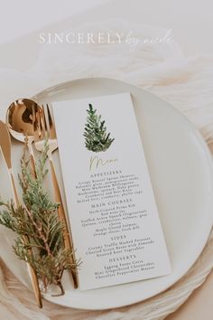 a table setting with place cards and gold utensils on it, along with greenery