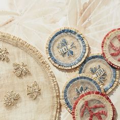 four embroidered bee coasters sitting on top of a white cloth covered tablecloth with red, white and blue designs