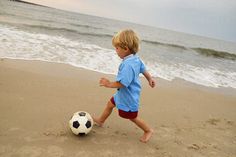 a little boy running on the beach with a soccer ball in his hand by the ocean