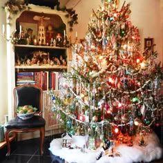 a decorated christmas tree in the corner of a room with a chair and bookshelf