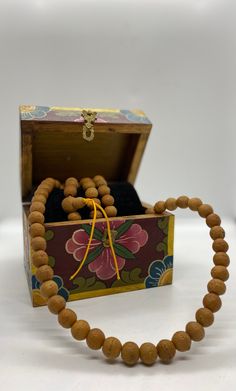 a wooden beaded necklace in a box on a white surface with a yellow ribbon