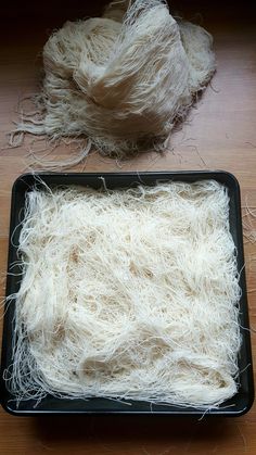 a black tray filled with white yarn on top of a wooden table next to a pile of wool