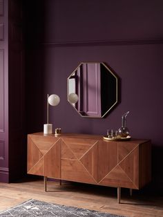 a room with purple walls and a large mirror on the wall above a wooden cabinet