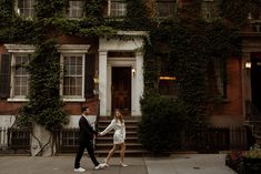 a man and woman walking in front of a building with ivy growing on the walls