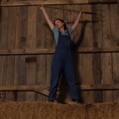 a woman standing on top of a hay bale in front of a wooden wall