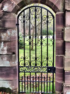 an iron gate in the middle of a brick wall with grass and trees behind it