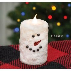 a white candle with a snowman face on it sitting next to a christmas tree