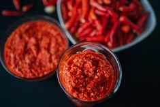 two bowls filled with red chili paste next to some peppers