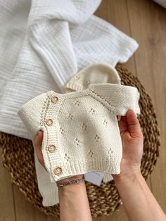 a person holding a white sweater on top of a wooden floor next to a basket