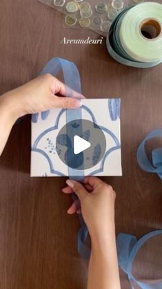 two hands holding a card with blue ribbon around it and some other items on the table