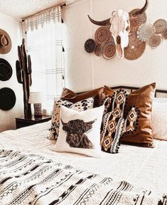 a bed topped with lots of pillows next to a wall mounted cow skull on the wall