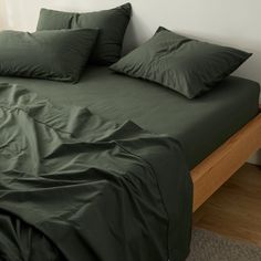 a bed with green sheets and pillows on top of it in a room next to a wall