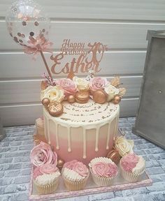 a pink and gold birthday cake with cupcakes on the bottom is decorated with flowers