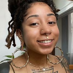 a woman with tattoos and piercings on her chest smiles at the camera while wearing large gold hoop earrings