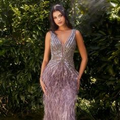 a woman in a long purple dress posing for the camera with trees and bushes behind her