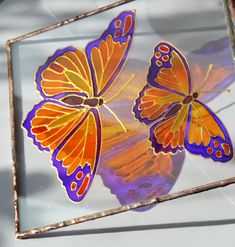 two orange and purple butterflies sitting on top of a glass plate with the reflection of another butterfly in it