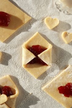 small pastries with jam in the middle on top of floured paper next to hearts