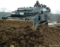 two men are riding on top of a tank in the mud while another man looks on