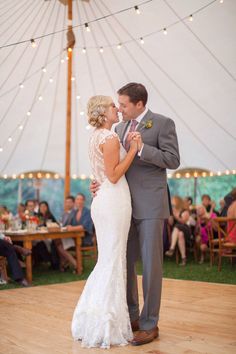 a bride and groom dance at their wedding reception under a tent with string lights in the background