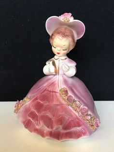 the figurine is wearing a pink dress and hat with gold trimmings