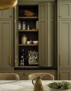 a kitchen with green cabinets and white marble counter tops, an open pantry door is in the center