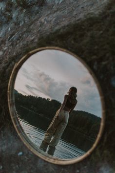 a woman standing in the water looking at her reflection in a mirror that is hanging on a rock