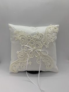 a white pillow with lace and ribbon on the front, sitting on a black stand