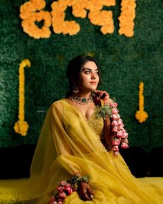 a woman in a yellow sari sitting on the ground with flowers around her neck