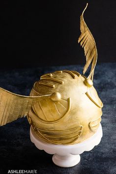 a gold fish sculpture sitting on top of a white pedestal next to a black wall