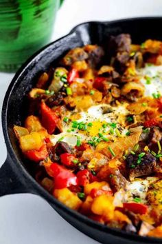 a skillet filled with lots of food on top of a white table next to a green cup