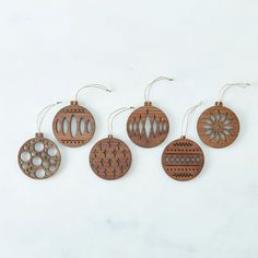 four wooden ornaments hanging from strings on a white surface, each decorated with an ornament