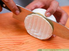 a person is cutting cheese with a large knife on a wooden table and it looks like they are about to slice