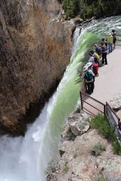 people are standing at the edge of a waterfall and looking down into the water below