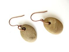 two brown stone earrings are hanging from copper hooks on a white surface with a black bead