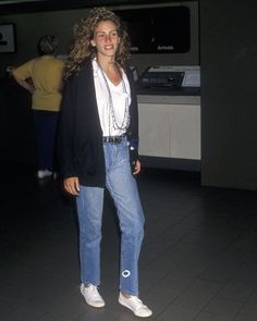 a woman standing in an airport wearing jeans and a blazer