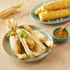 corn on the cob and dipping sauces are sitting on two plates, next to each other