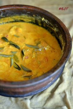 a brown bowl filled with yellow soup on top of a cloth covered table next to a wooden spoon