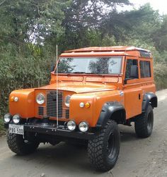 an orange land rover is parked on the side of the road in front of some trees